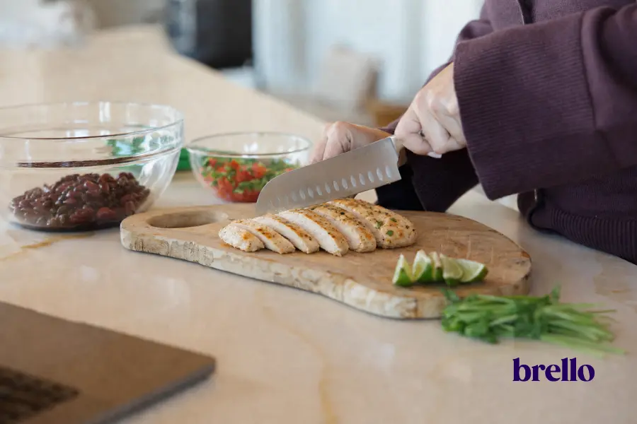 Woman cutting cooked chicken breast into cubes.