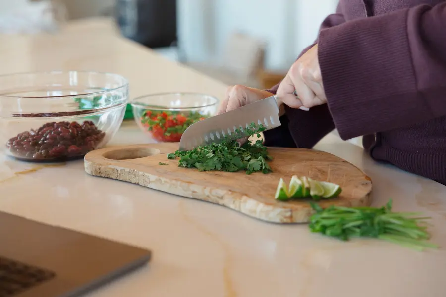 Hands chopping fresh herbs on a cutting board beside bowls of beans and chopped vegetables