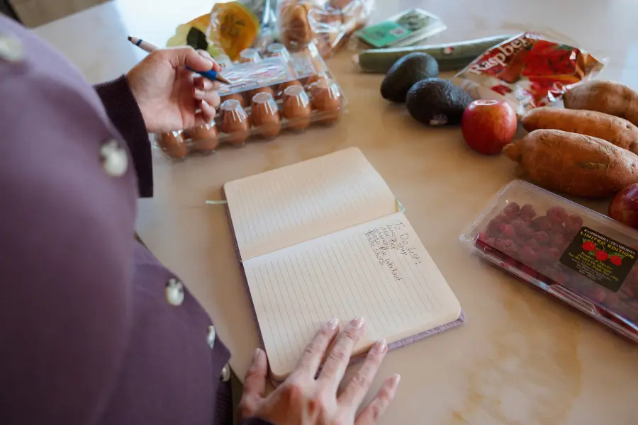Hands planning meals in a notebook next to eggs and fresh produce